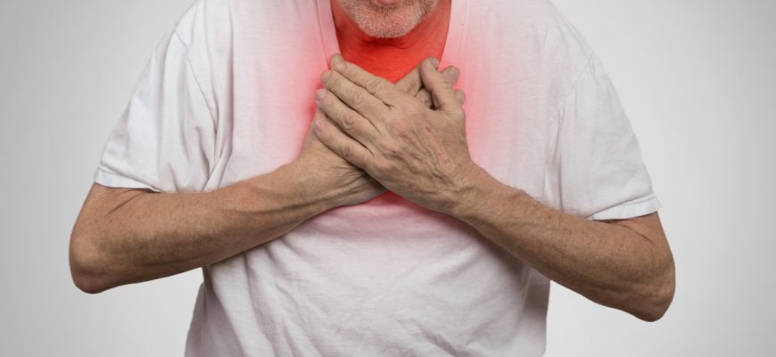 Male senior citizen holds his hands onto his chest in pain.